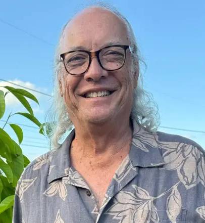Smiling man with glasses wearing a floral shirt, standing outdoors among greenery, representing the Tax Relief Heroes team.